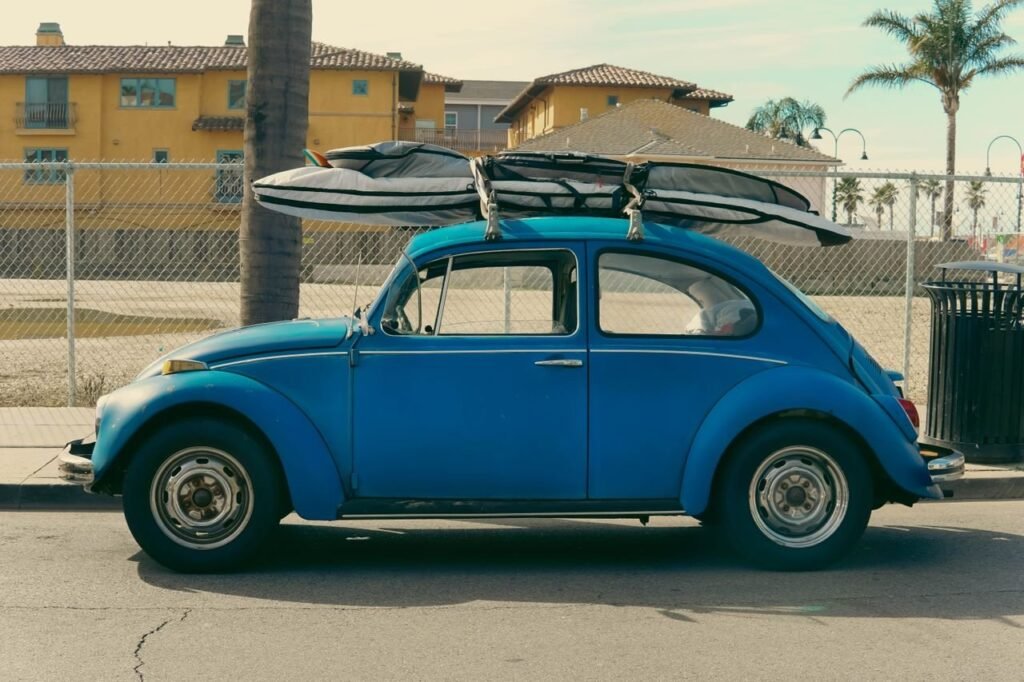 A classic blue Volkswagen Beetle with surfboards parked by a sunny beachside in California.
